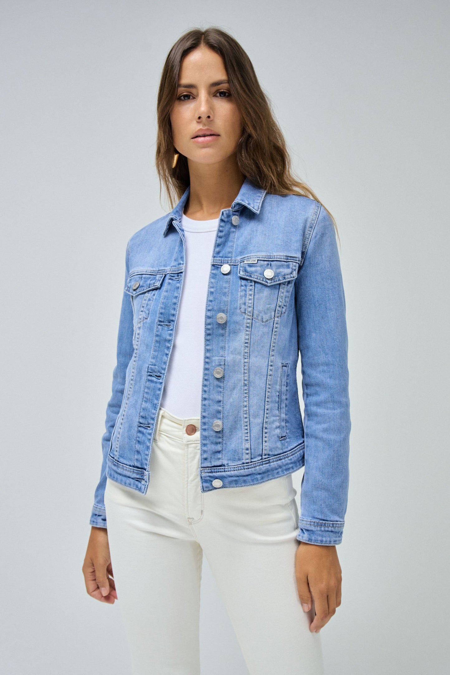 Woman wearing a blue denim jacket over a white shirt and pants on a gray background