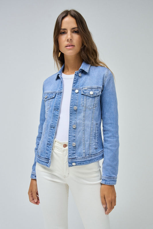 Woman wearing a blue denim jacket over a white shirt and pants on a gray background