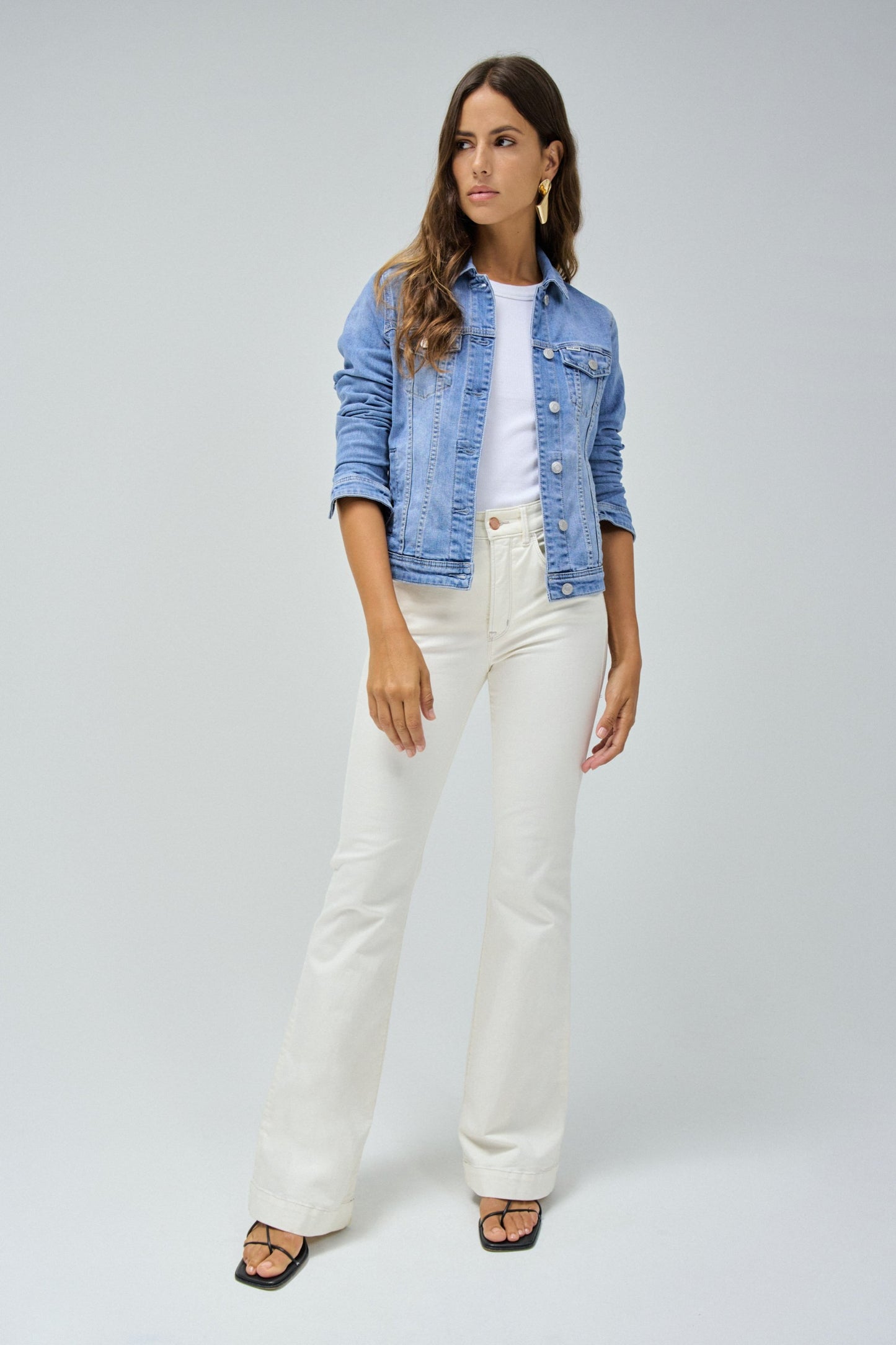 Woman wearing a denim jacket and white pants on a plain background