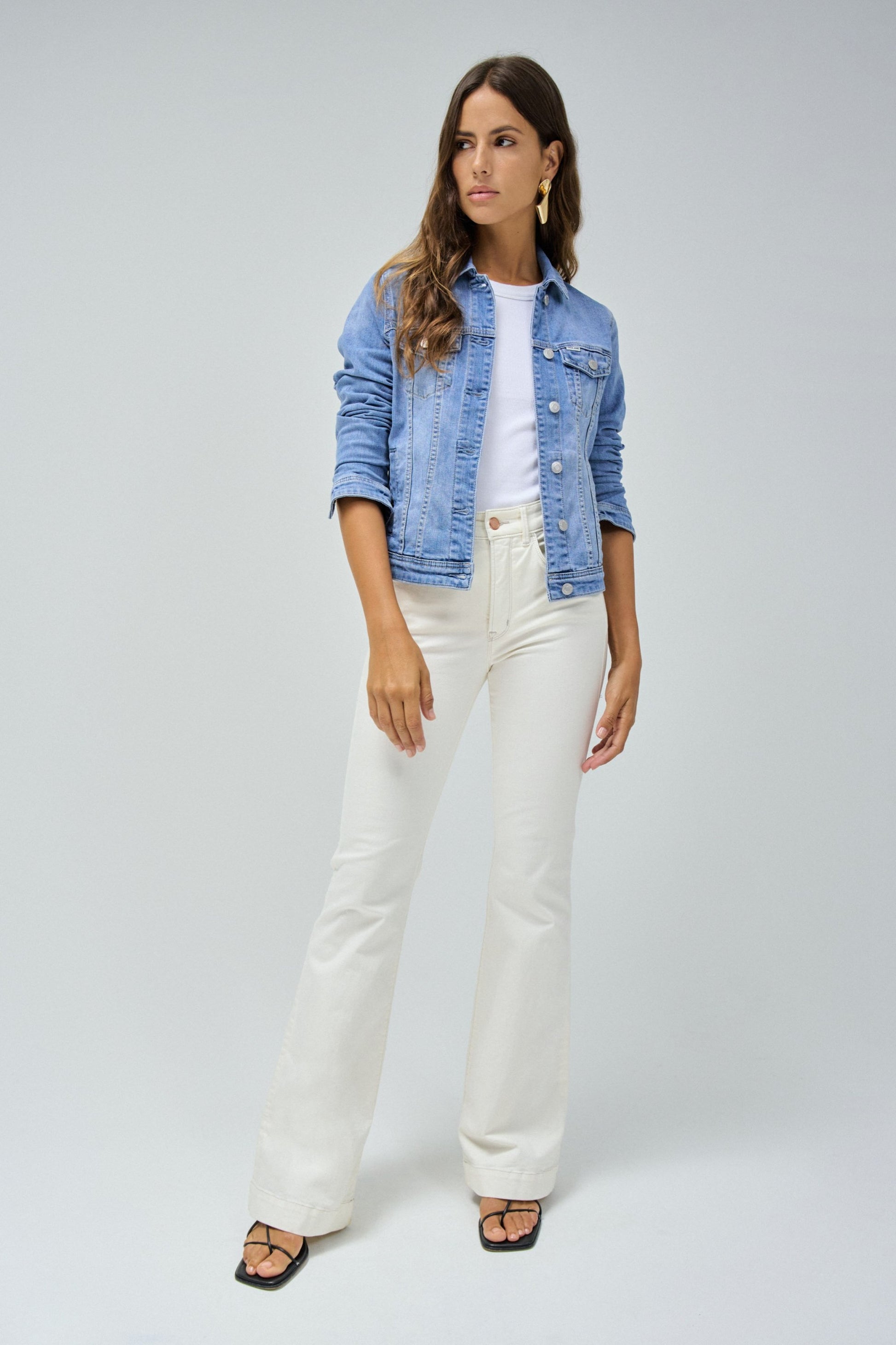 Woman wearing a denim jacket and white pants on a plain background