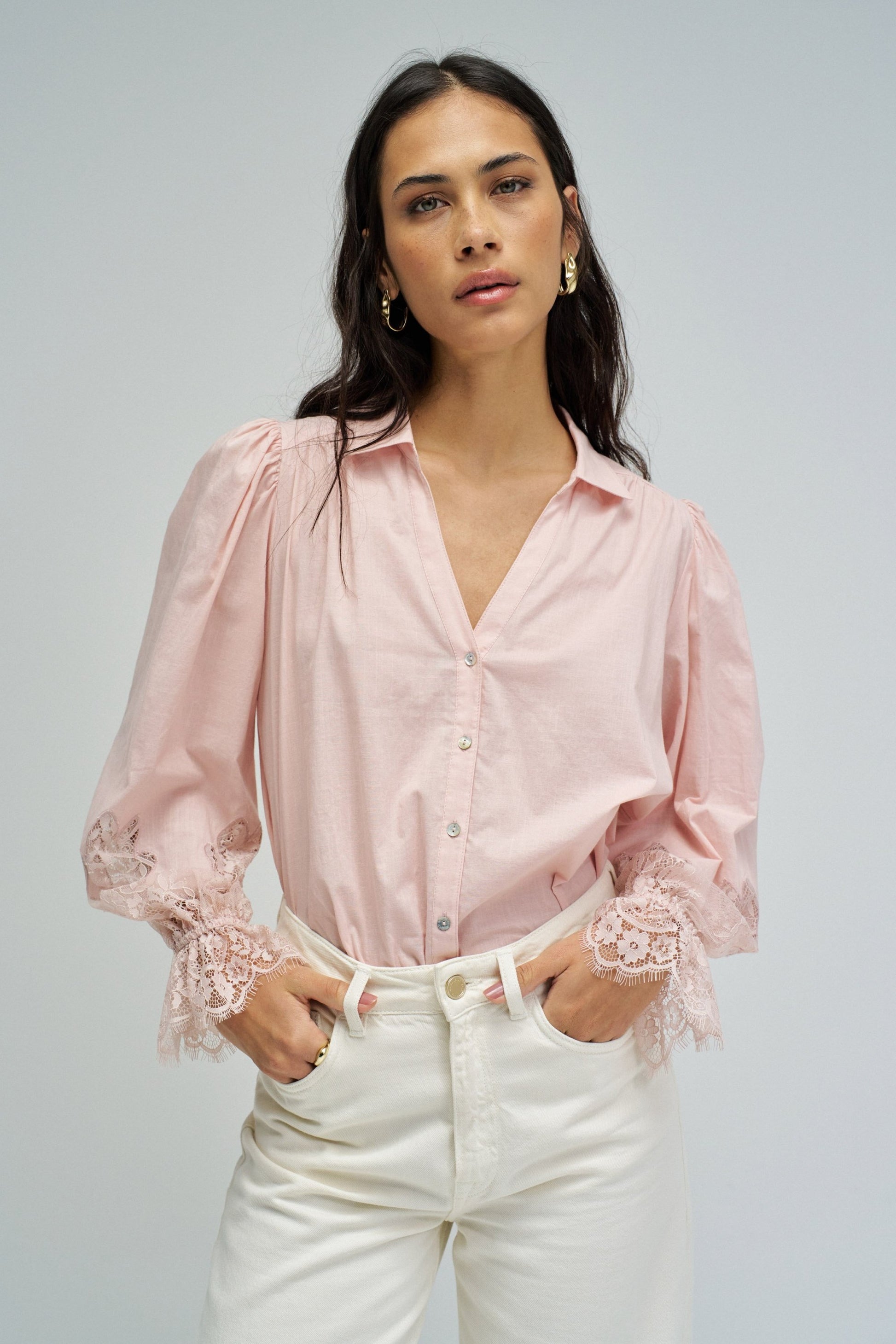 Woman wearing a pink blouse with lace details on a gray background