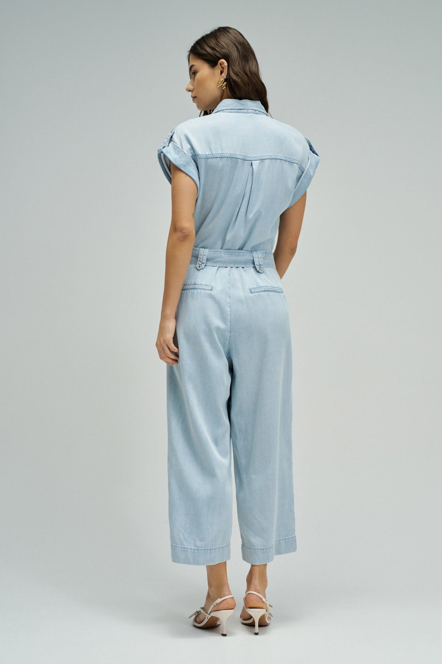 Woman wearing a light blue denim jumpsuit on a plain background