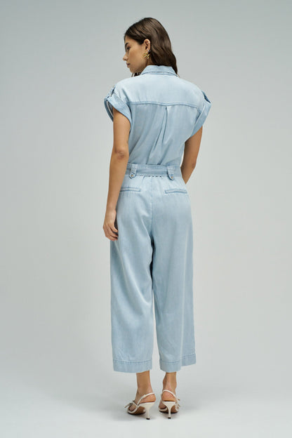 Woman wearing a light blue denim jumpsuit on a plain background