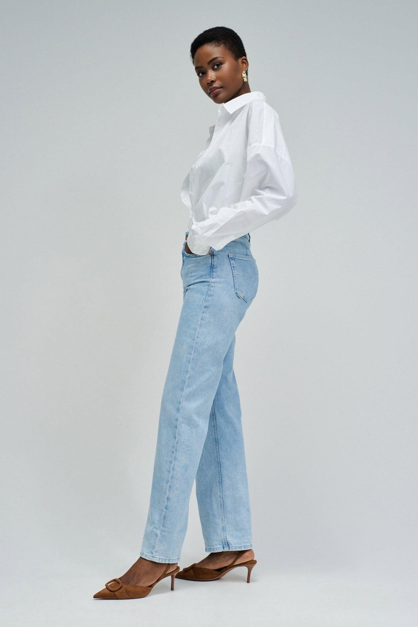 Woman wearing a white shirt and light blue jeans on a gray background