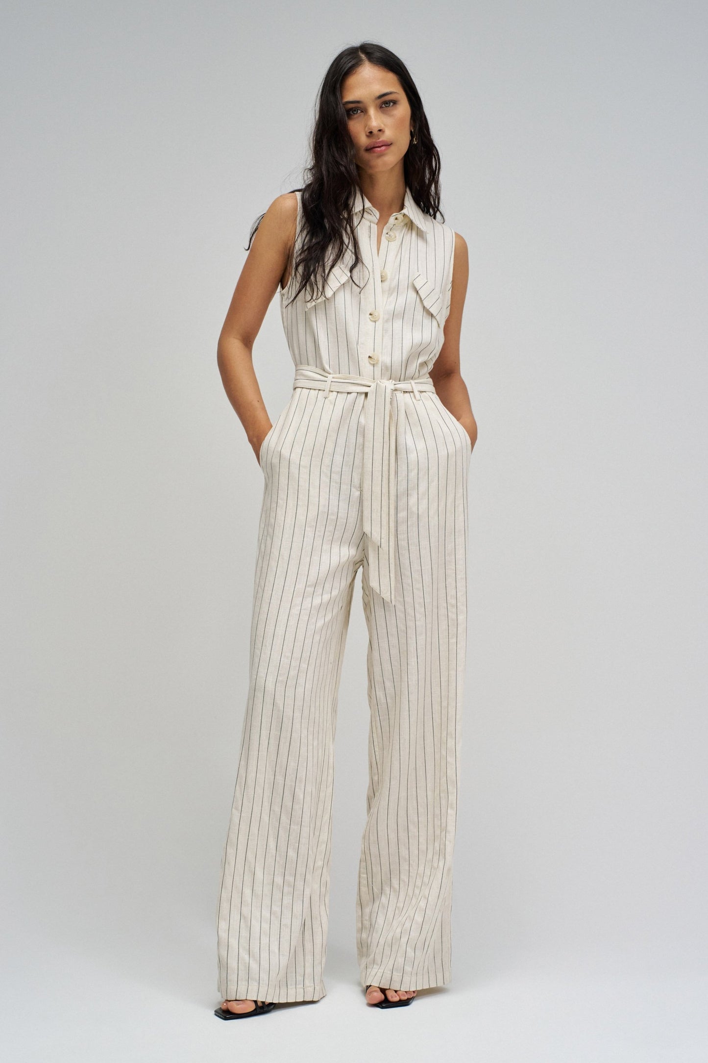 Woman wearing a white pinstripe jumpsuit on a plain background