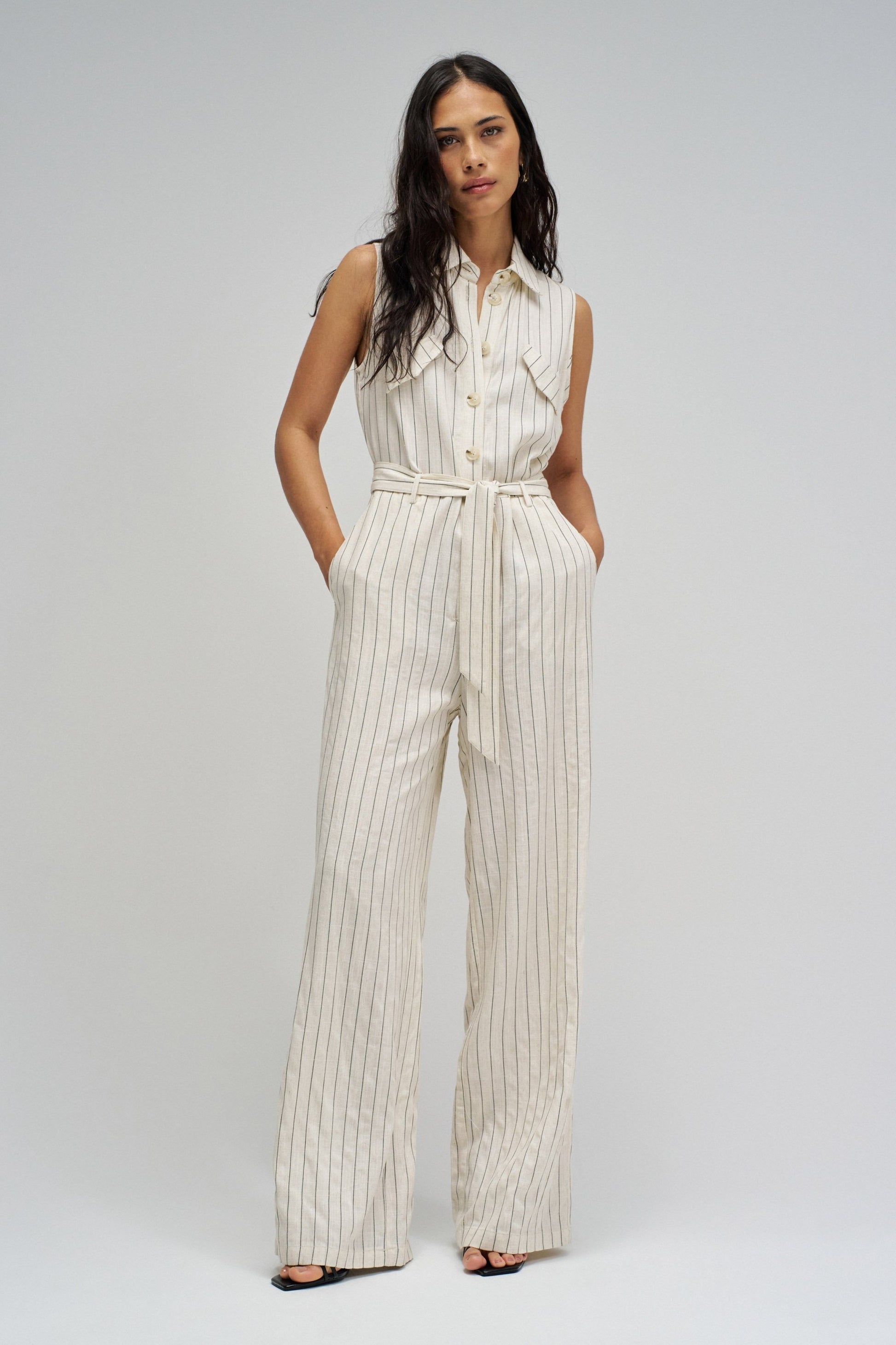 Woman wearing a white pinstripe jumpsuit on a plain background