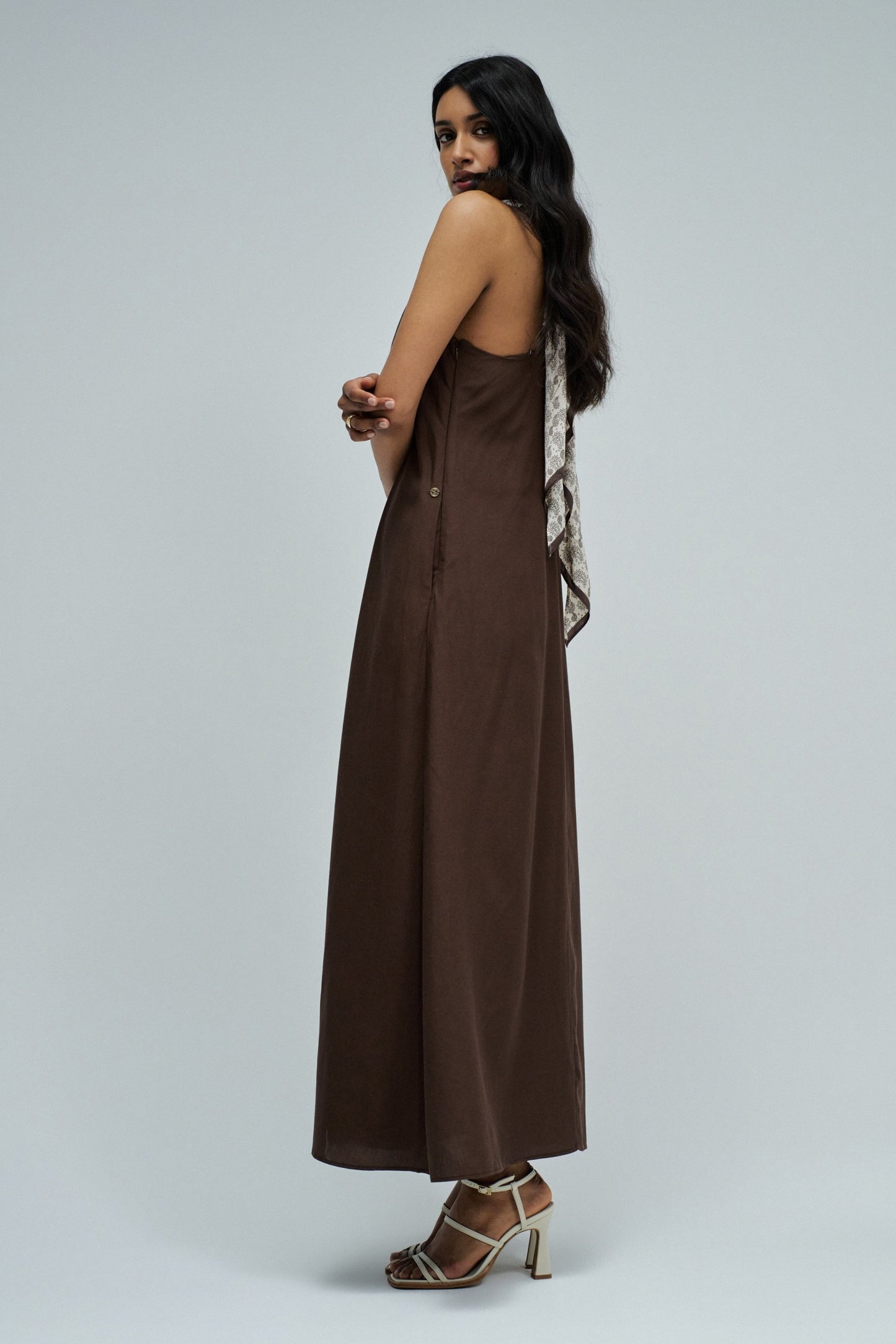 Woman wearing a long brown dress on a plain background