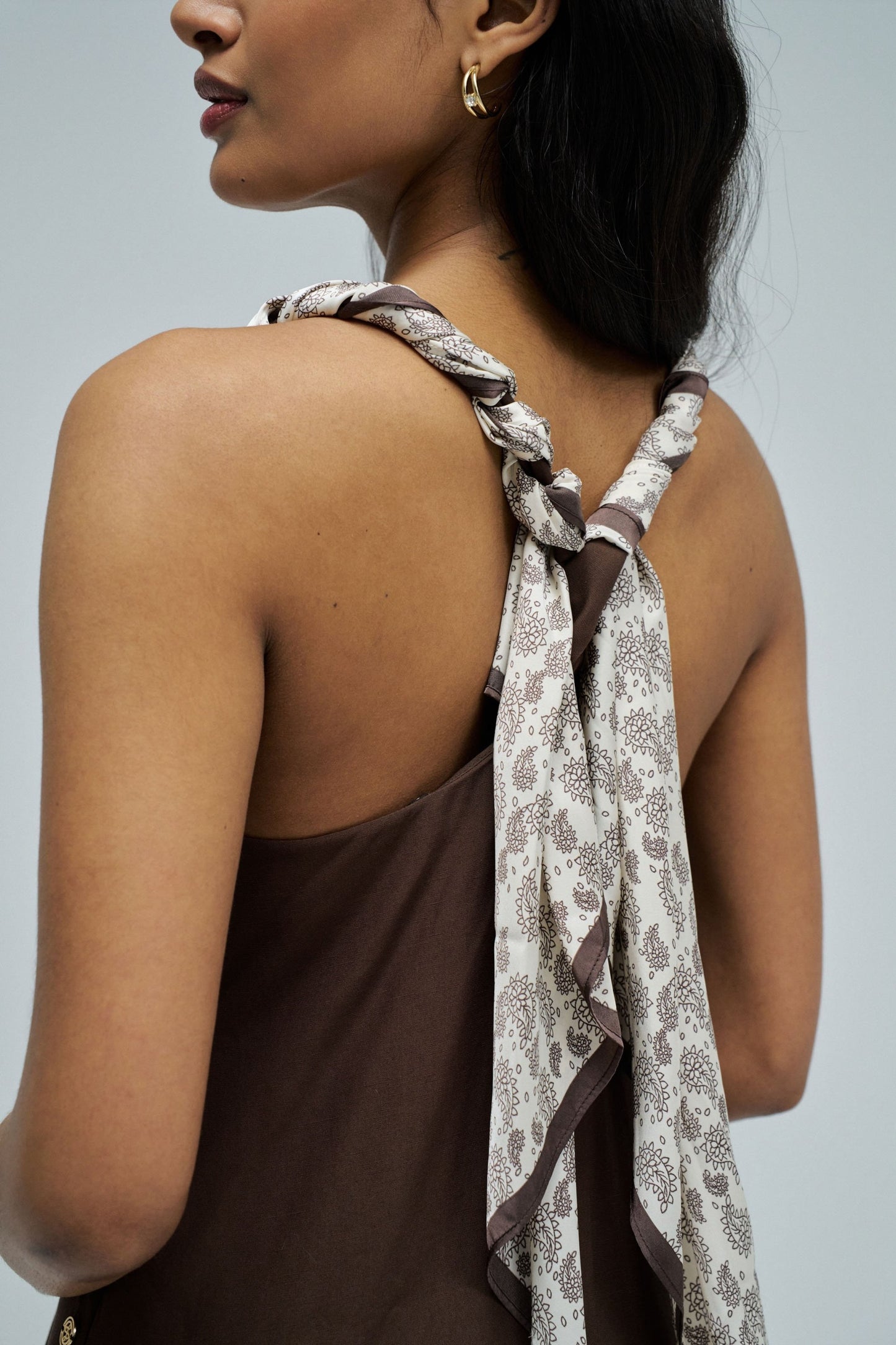 Woman wearing a brown top with a floral scarf over her shoulder against a gray background