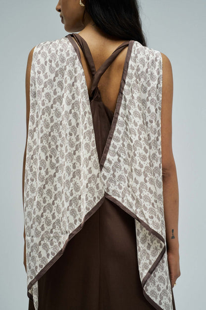 Woman wearing a patterned beige and brown scarf over a brown dress on a gray background