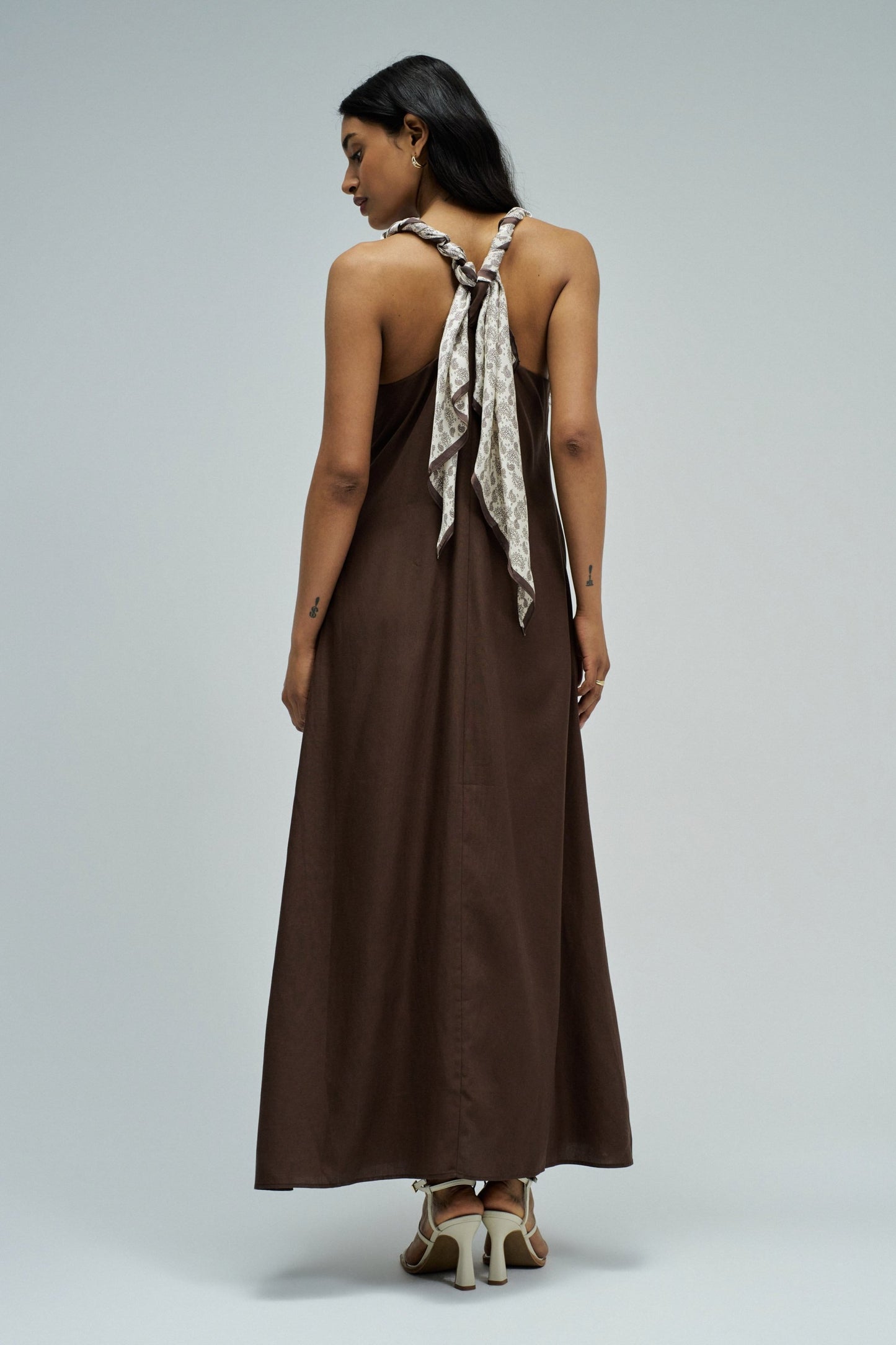 Woman wearing a brown dress with a scarf on a plain background