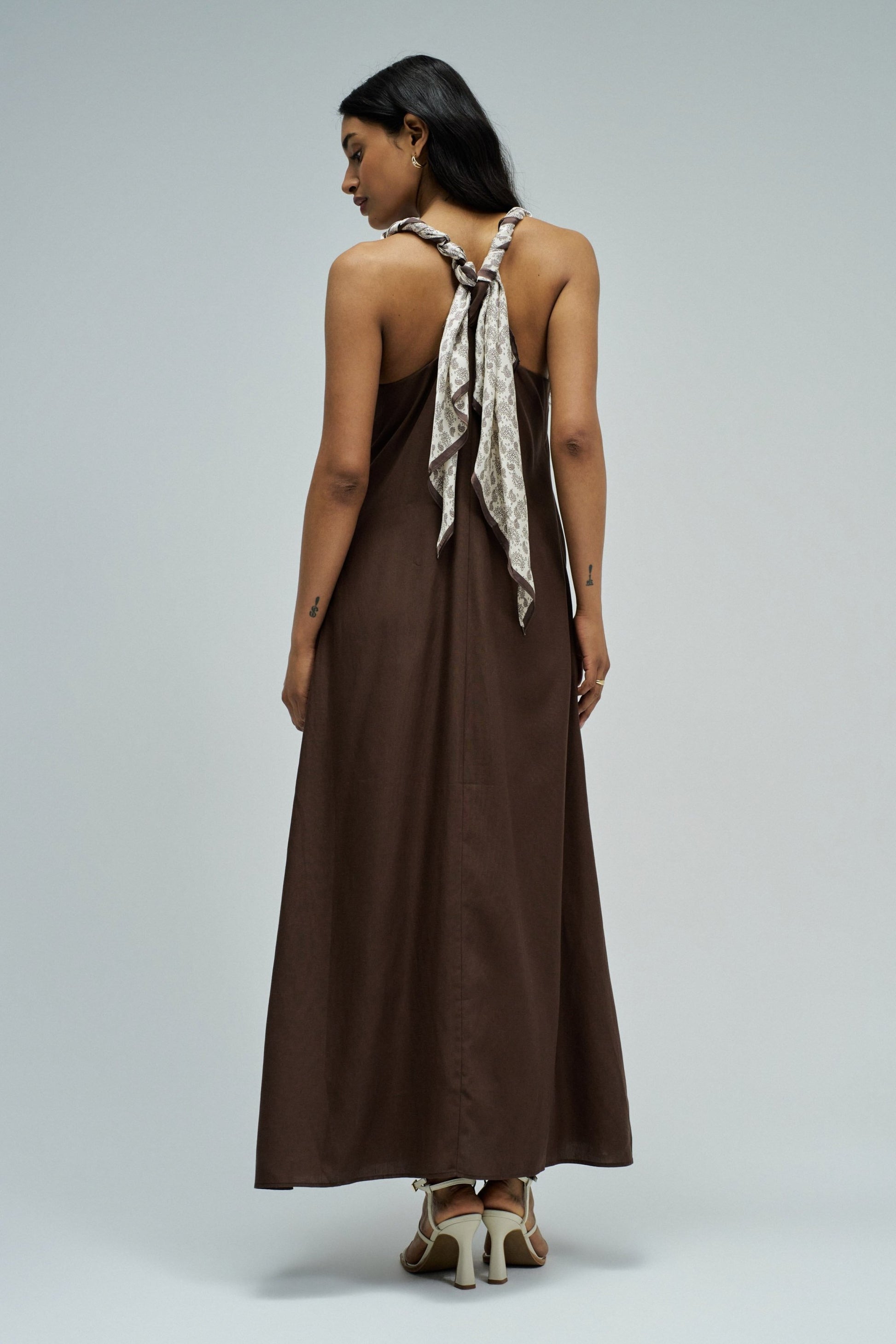 Woman wearing a brown dress with a scarf on a plain background