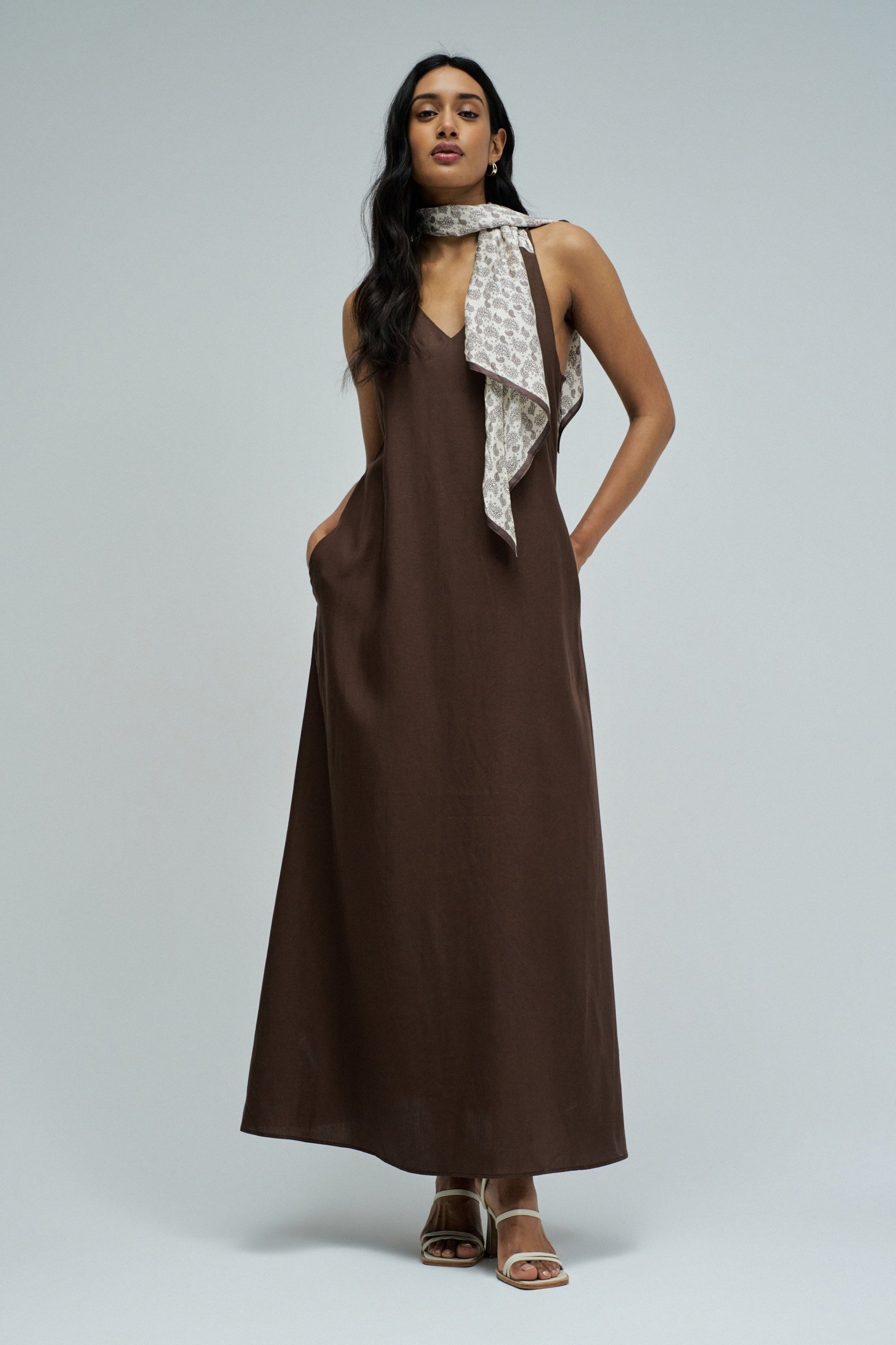 Woman wearing a brown dress with a patterned scarf on a gray background