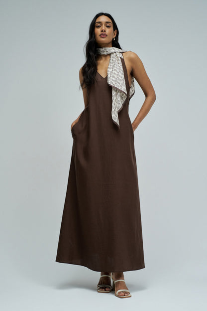 Woman wearing a brown dress with a patterned scarf on a gray background