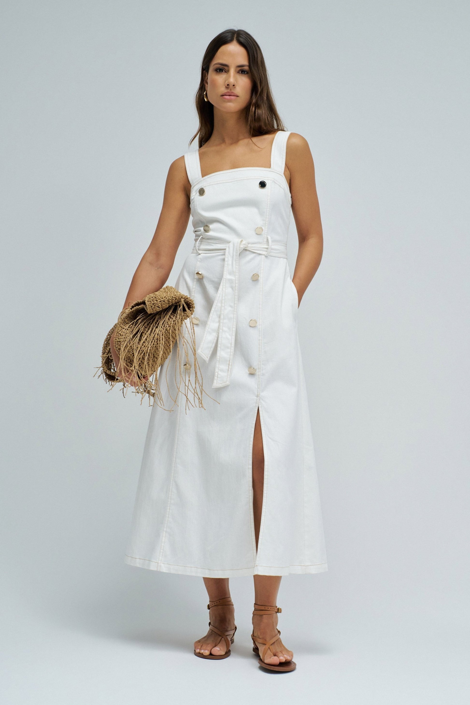 Woman wearing a white dress with a straw bag on a plain background