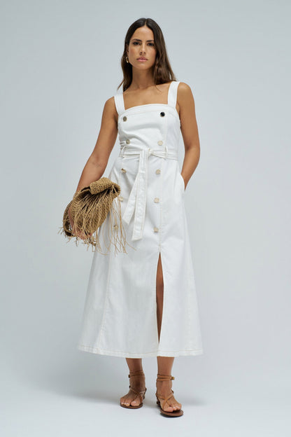 Woman wearing a white dress with a straw bag on a plain background