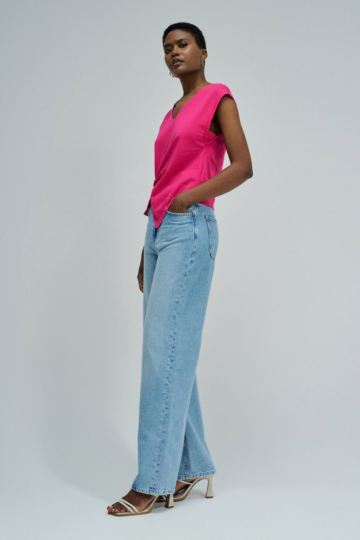 Woman wearing a bright pink sleeveless top and light blue jeans on a plain background