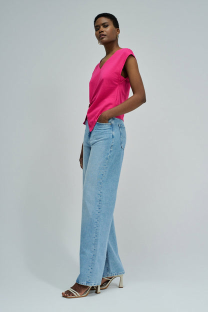 Woman wearing a bright pink sleeveless top and light blue jeans on a plain background