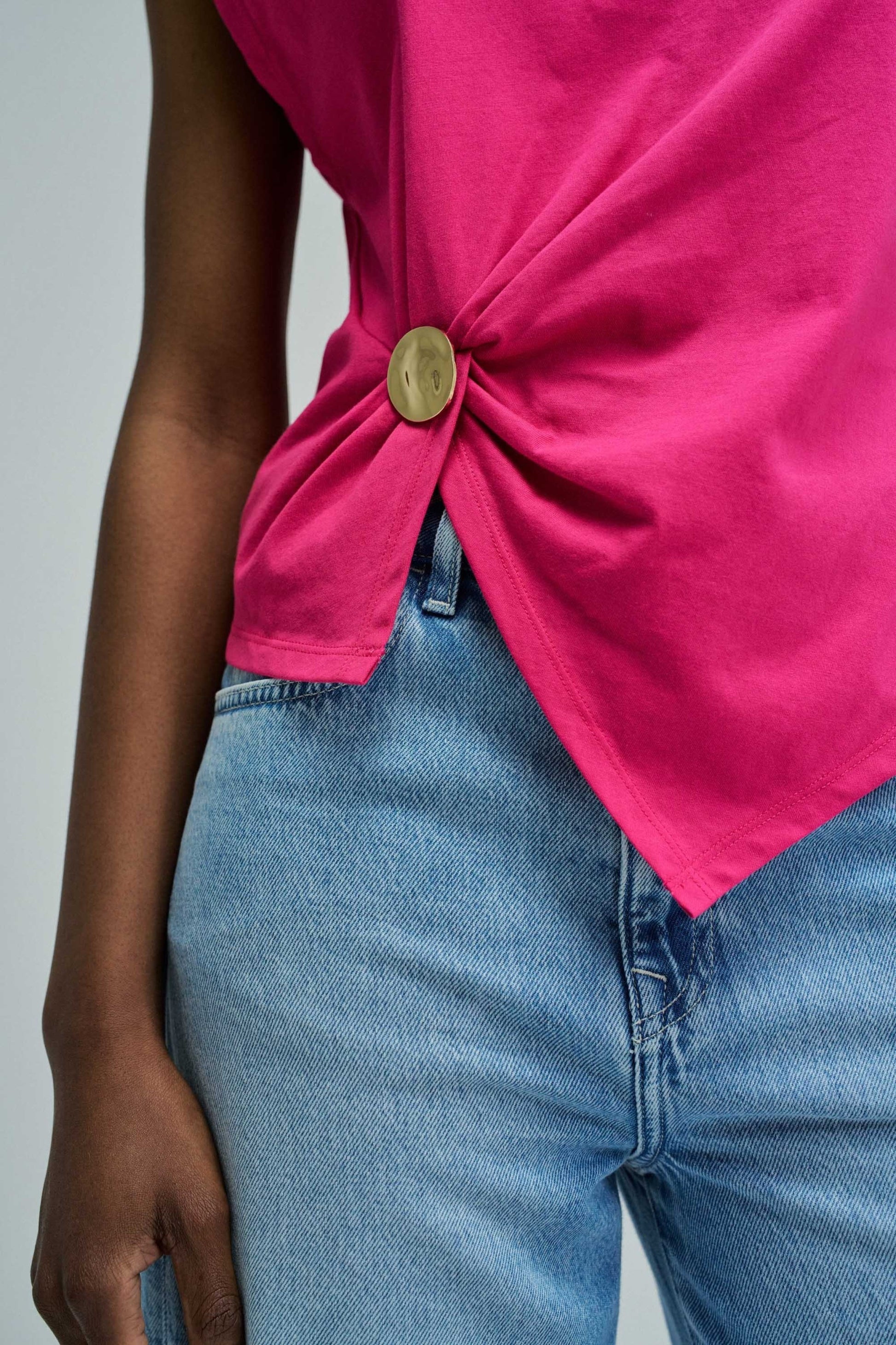 Person wearing a bright pink top with a knot detail and blue jeans on a gray background