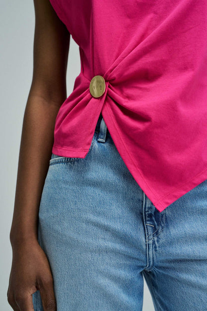Person wearing a bright pink top with a knot detail and blue jeans on a gray background