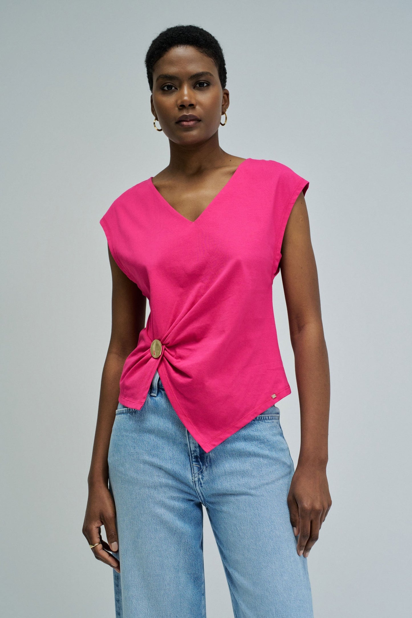 Woman wearing a bright pink top with a knot detail and light blue jeans on a gray background