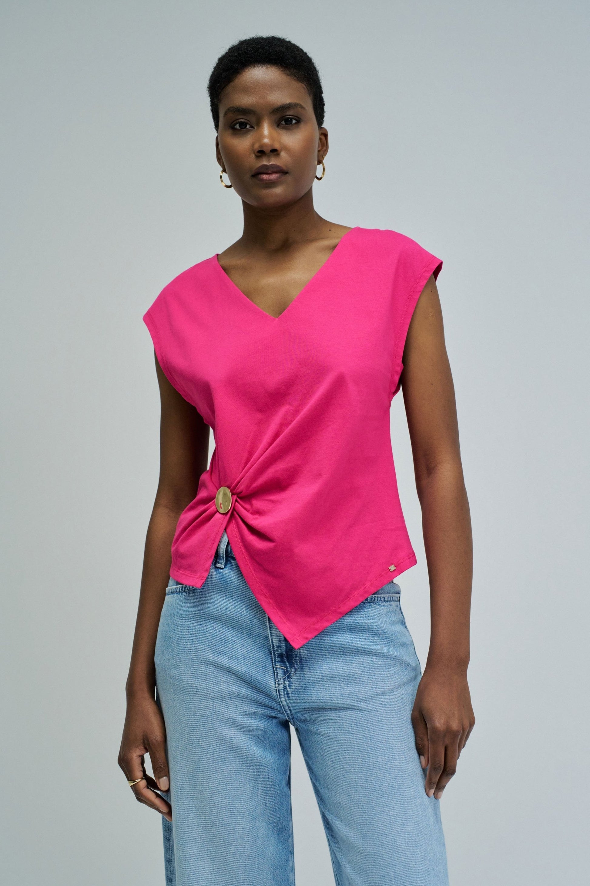 Woman wearing a bright pink top with a knot detail and light blue jeans on a gray background