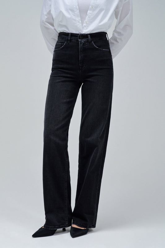 A person wearing black wide-leg jeans with a white button-up shirt tucked in and black pointed shoes, photographed against a light gray studio background.