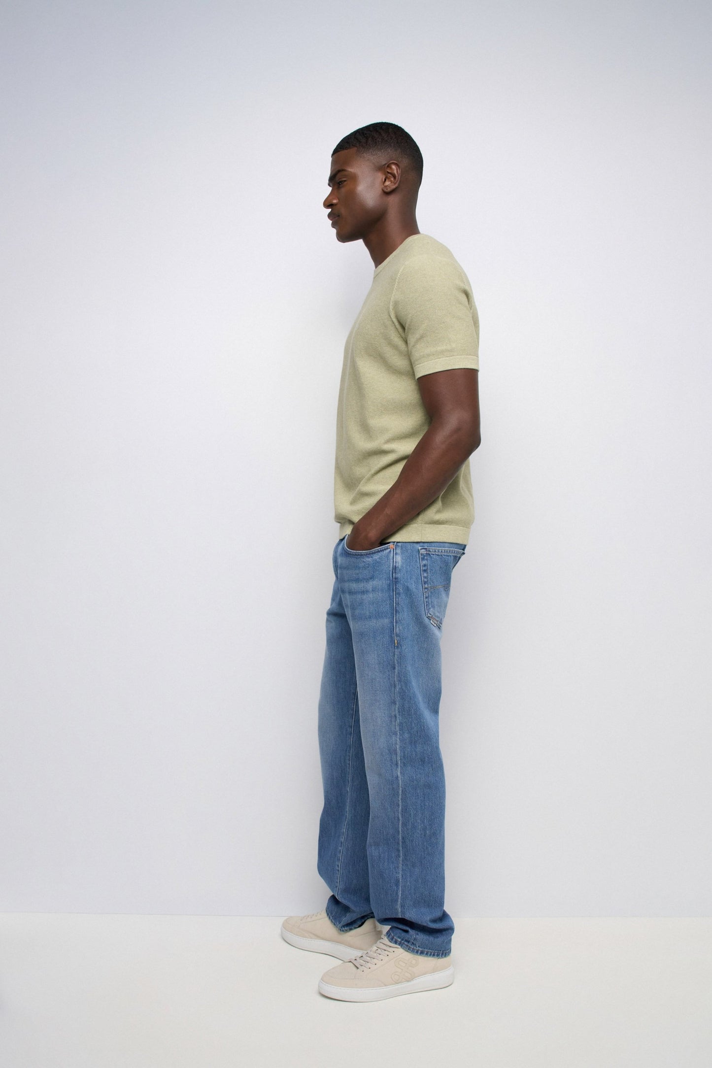 Man wearing a light green t-shirt and blue jeans standing against a white background