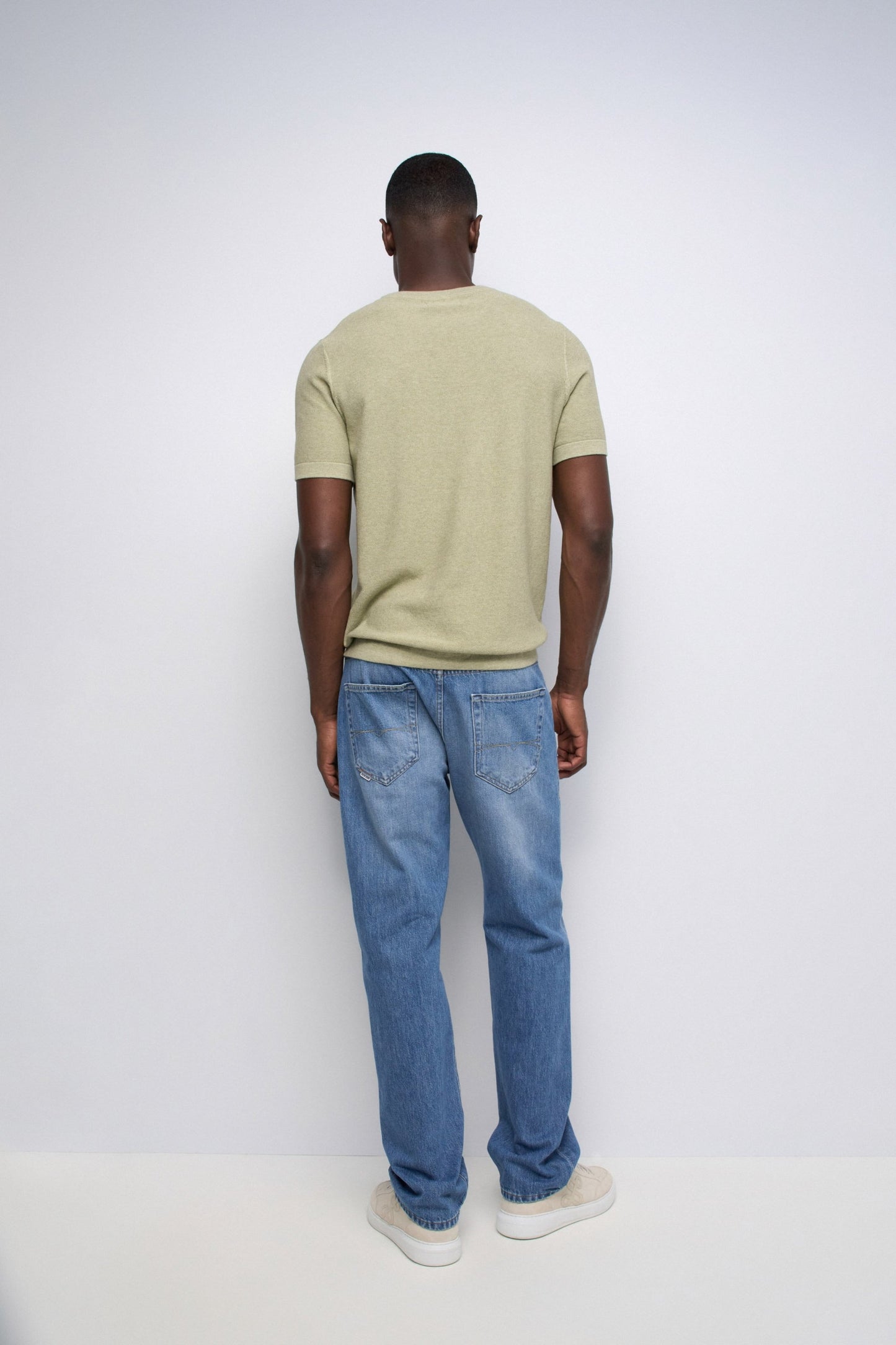 Person wearing a light green t-shirt and blue jeans on a white background