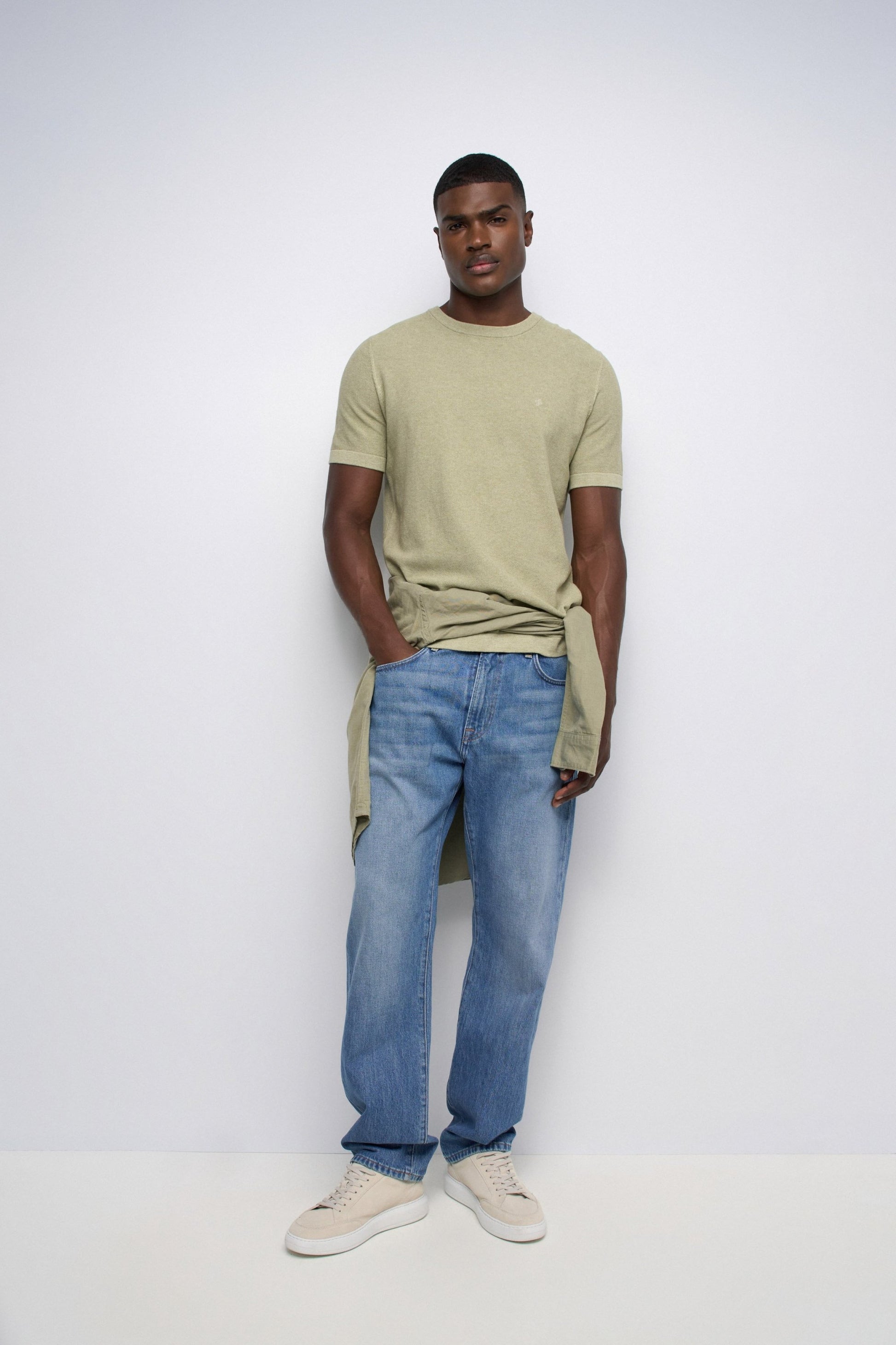 Man wearing a green t-shirt and blue jeans against a white background