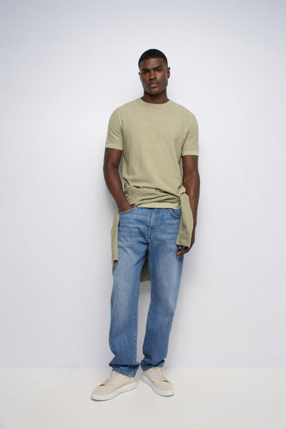 Man wearing a green t-shirt and blue jeans against a white background
