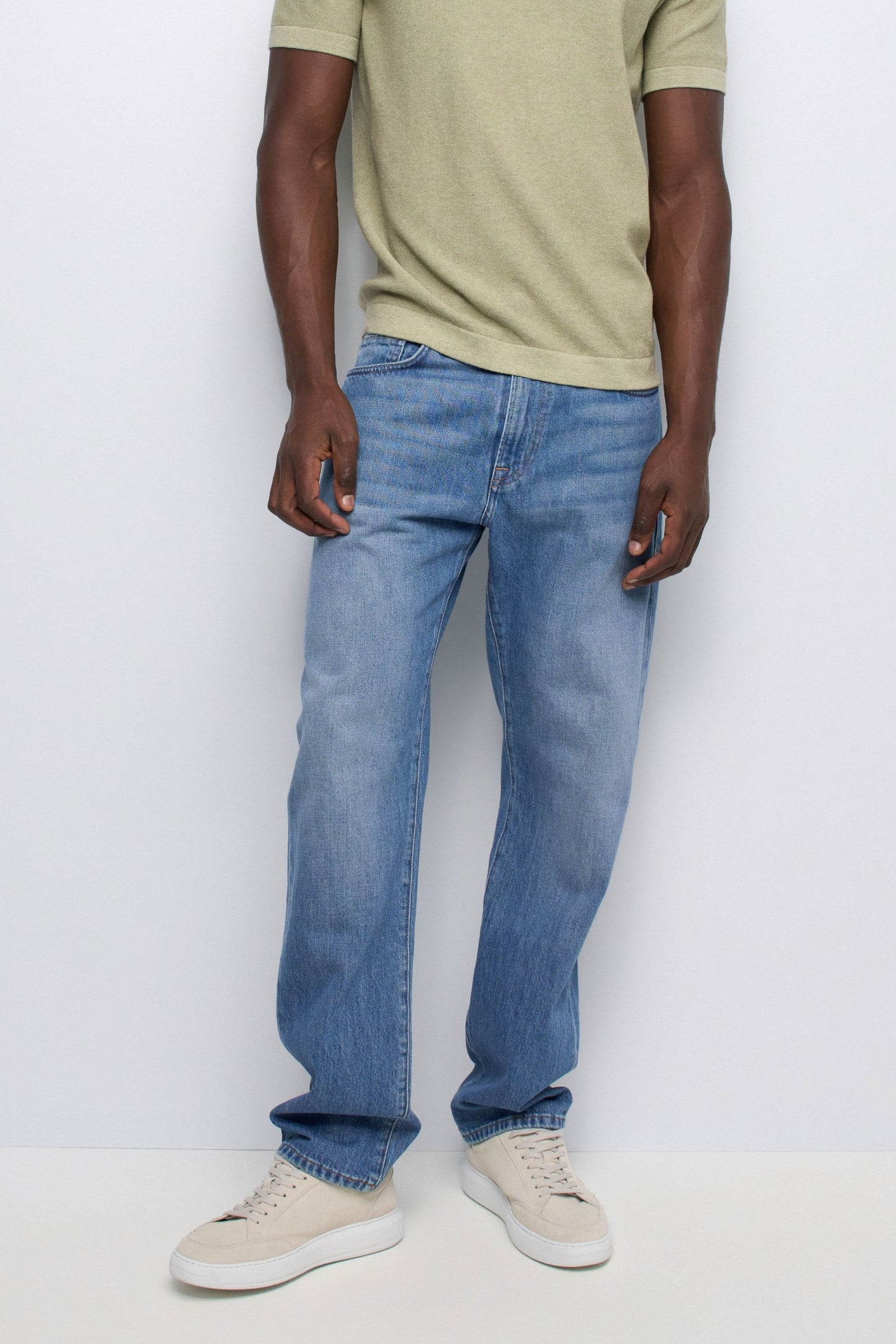 Person wearing light blue jeans and a beige shirt against a white background