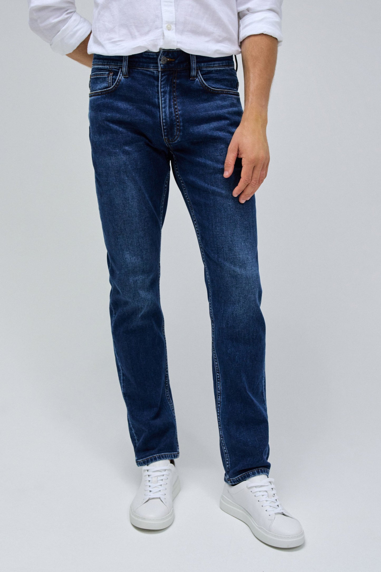 Person wearing blue jeans and white sneakers on a plain background
