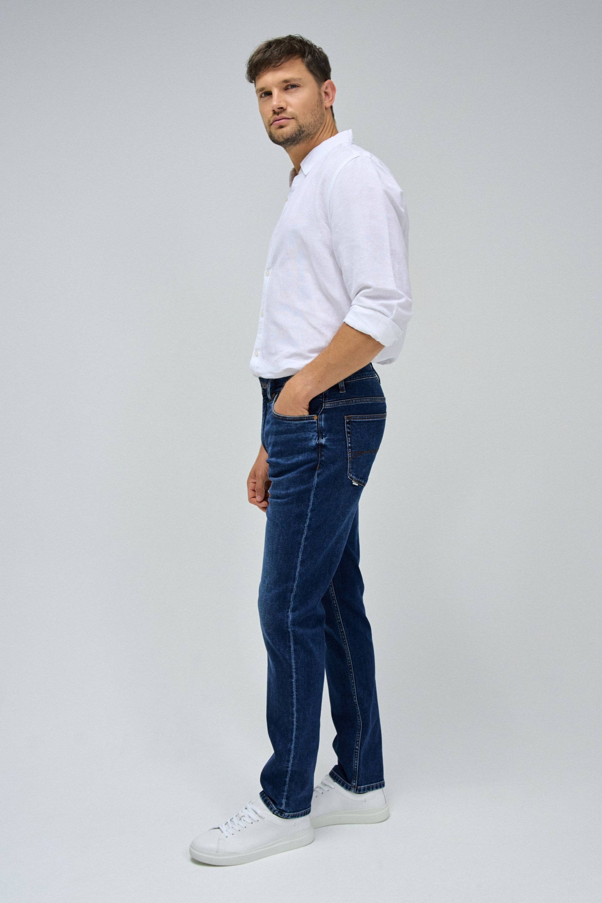 Man wearing a white sweater and blue jeans on a gray background