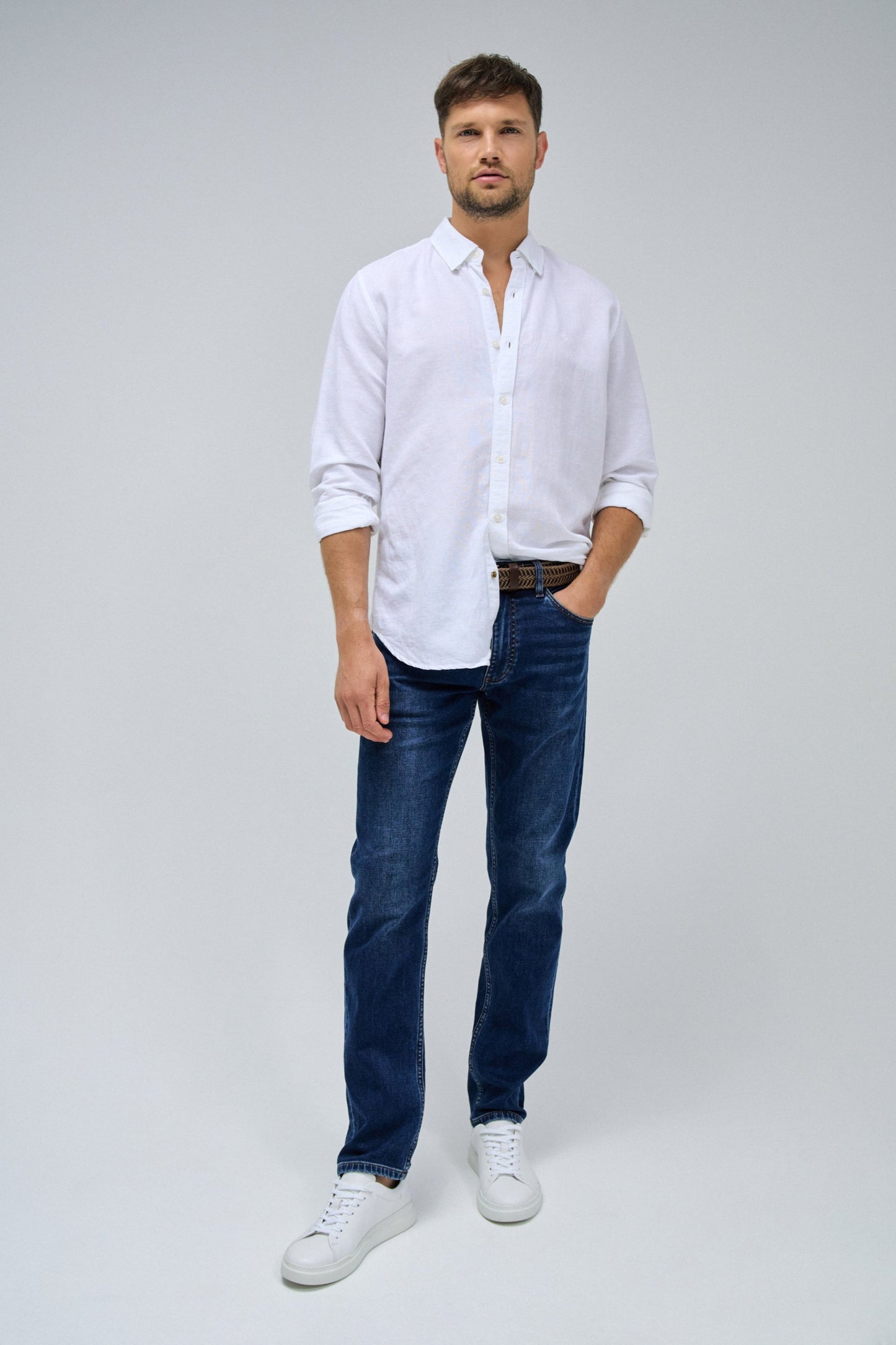 Man wearing a white shirt, blue jeans, and white sneakers on a gray background