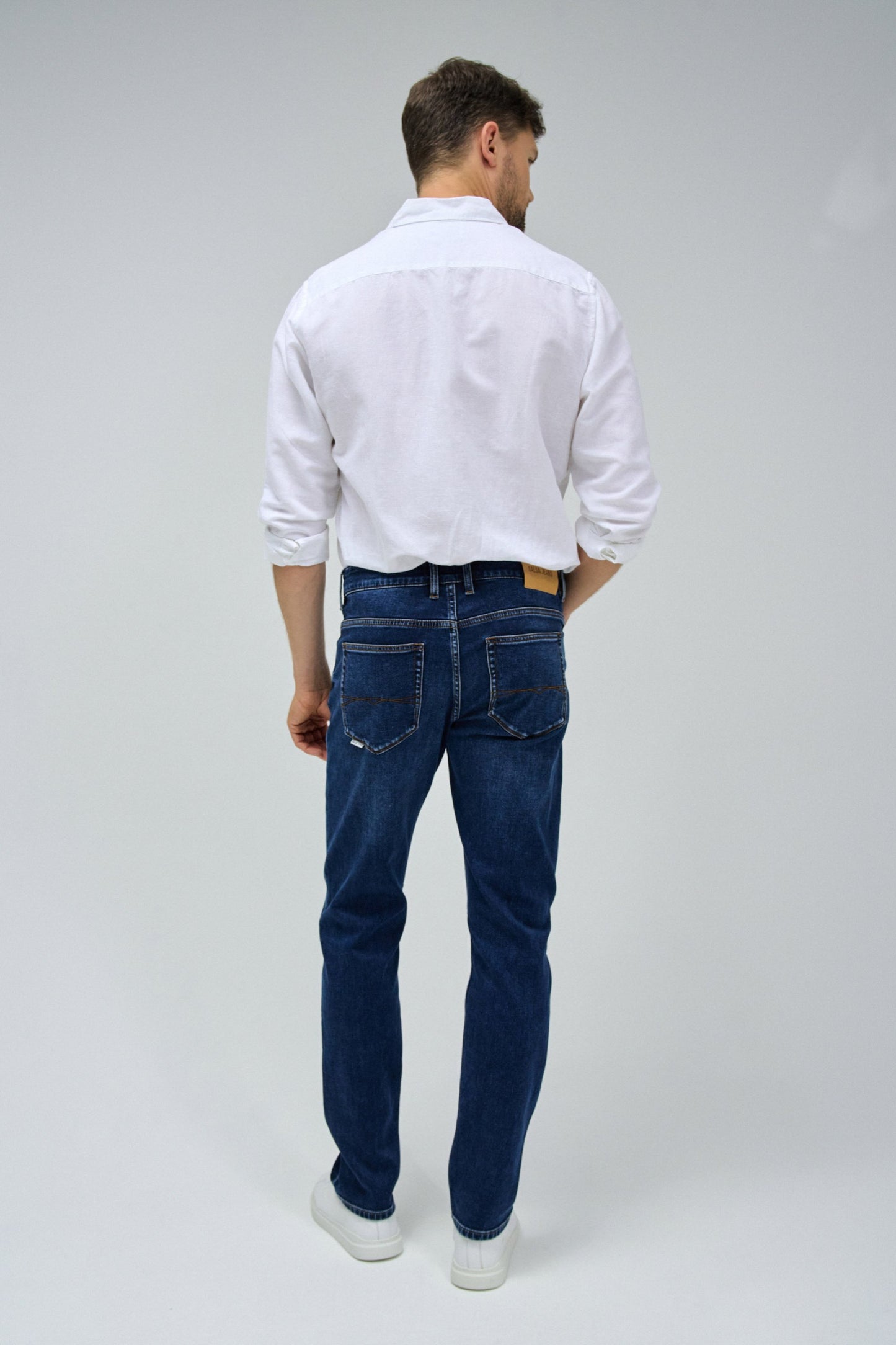 Man wearing a white shirt and blue jeans on a gray background