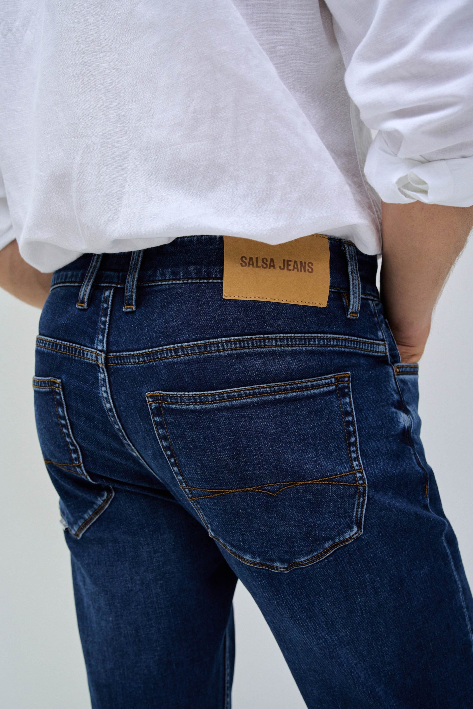 Person wearing blue jeans with a visible brand label on a plain background