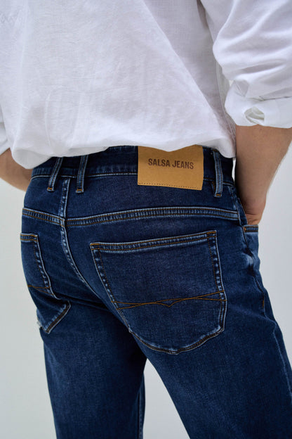 Person wearing blue jeans with a visible brand label on a plain background