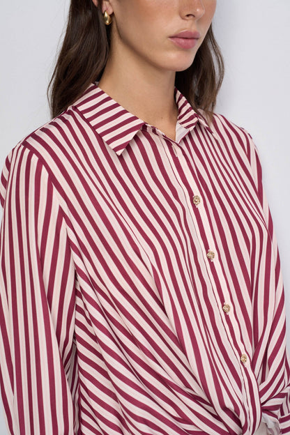 A close-up of a woman wearing a collared button-front blouse with diagonal stripes in burgundy and off-white, paired with gold-tone buttons.