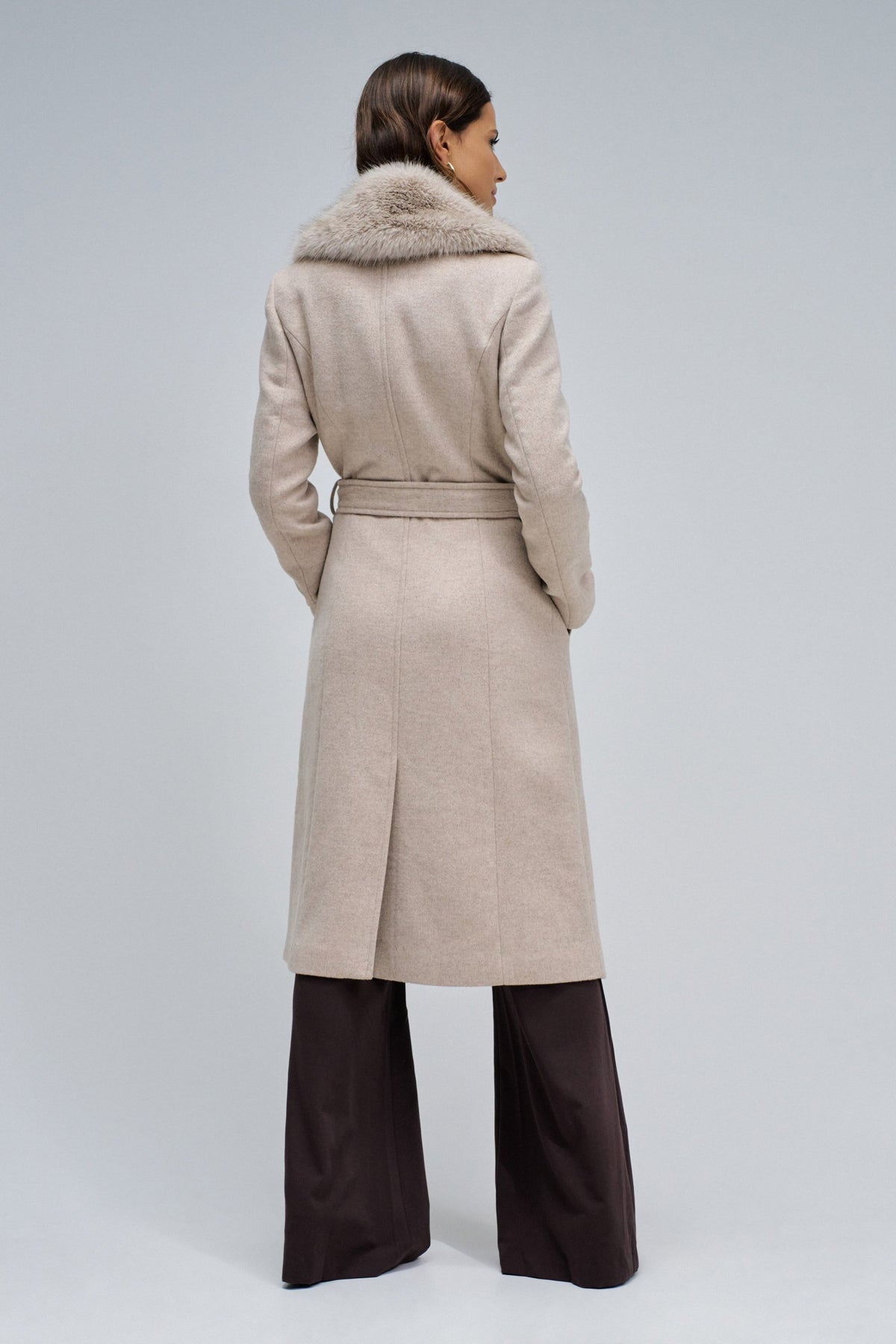 Woman wearing a beige coat with a fur collar on a white background