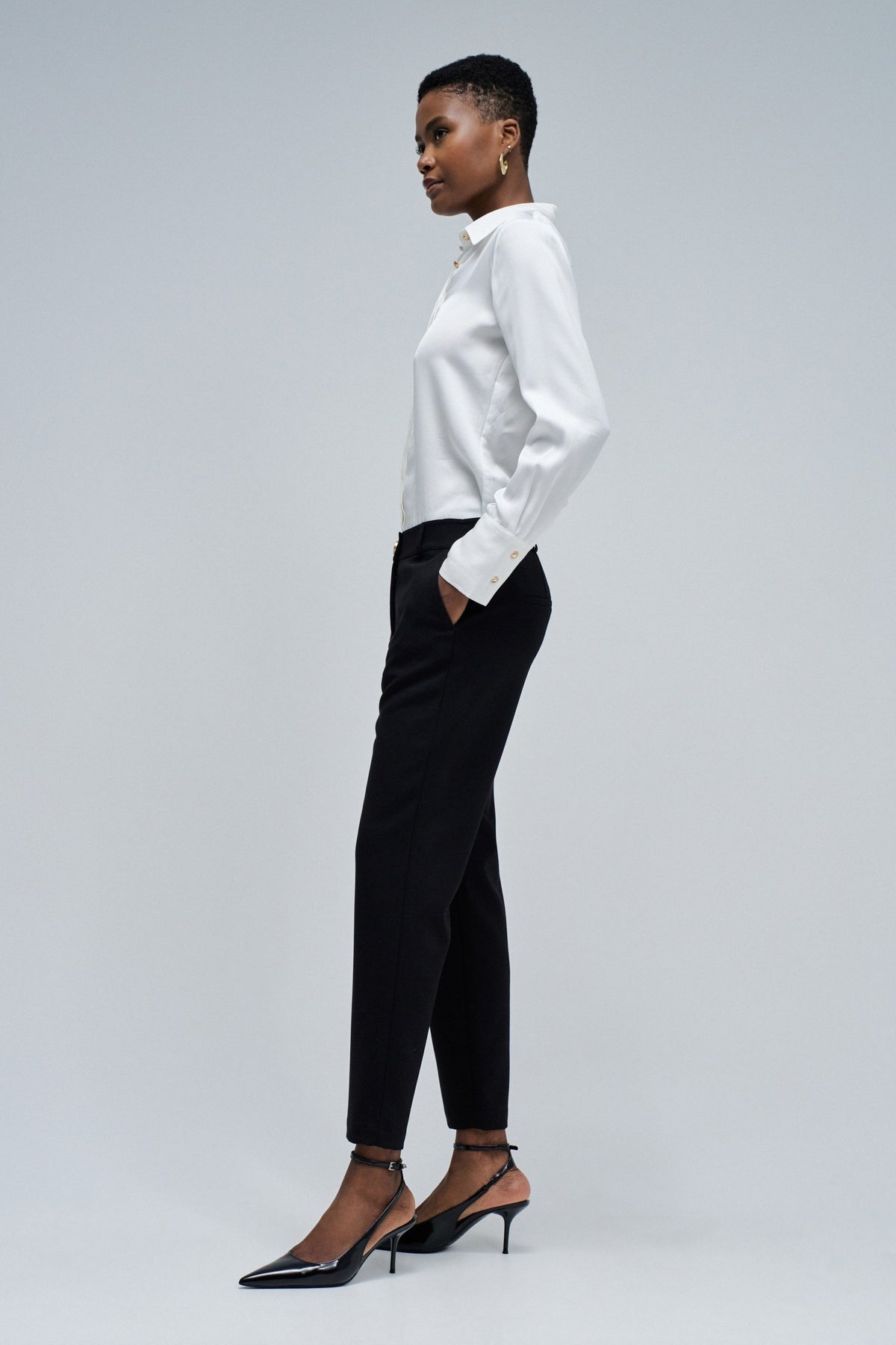 Woman wearing a white blouse and black pants on a gray background