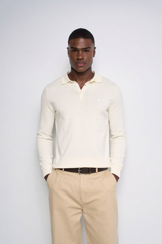A man wearing a cream long-sleeve polo shirt and beige trousers, standing against a light gray studio background.