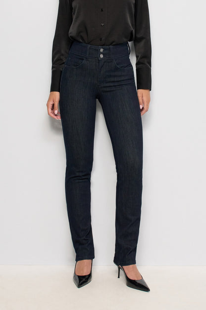 A model wearing dark wash slim-fit jeans, a black long-sleeve button-up shirt, and black patent leather high heels, standing against a plain white studio background.
