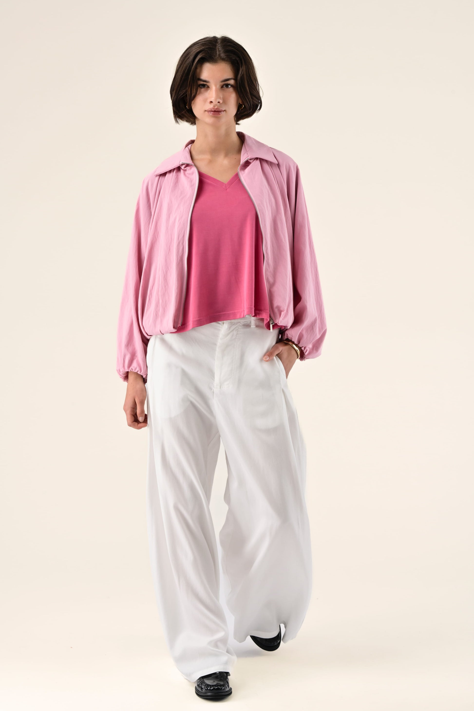 Person wearing a pink jacket, pink shirt, and white pants on a light background