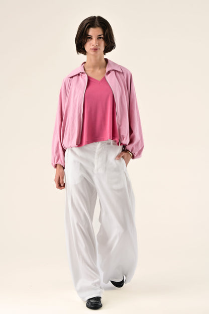 Person wearing a pink jacket, pink shirt, and white pants on a light background