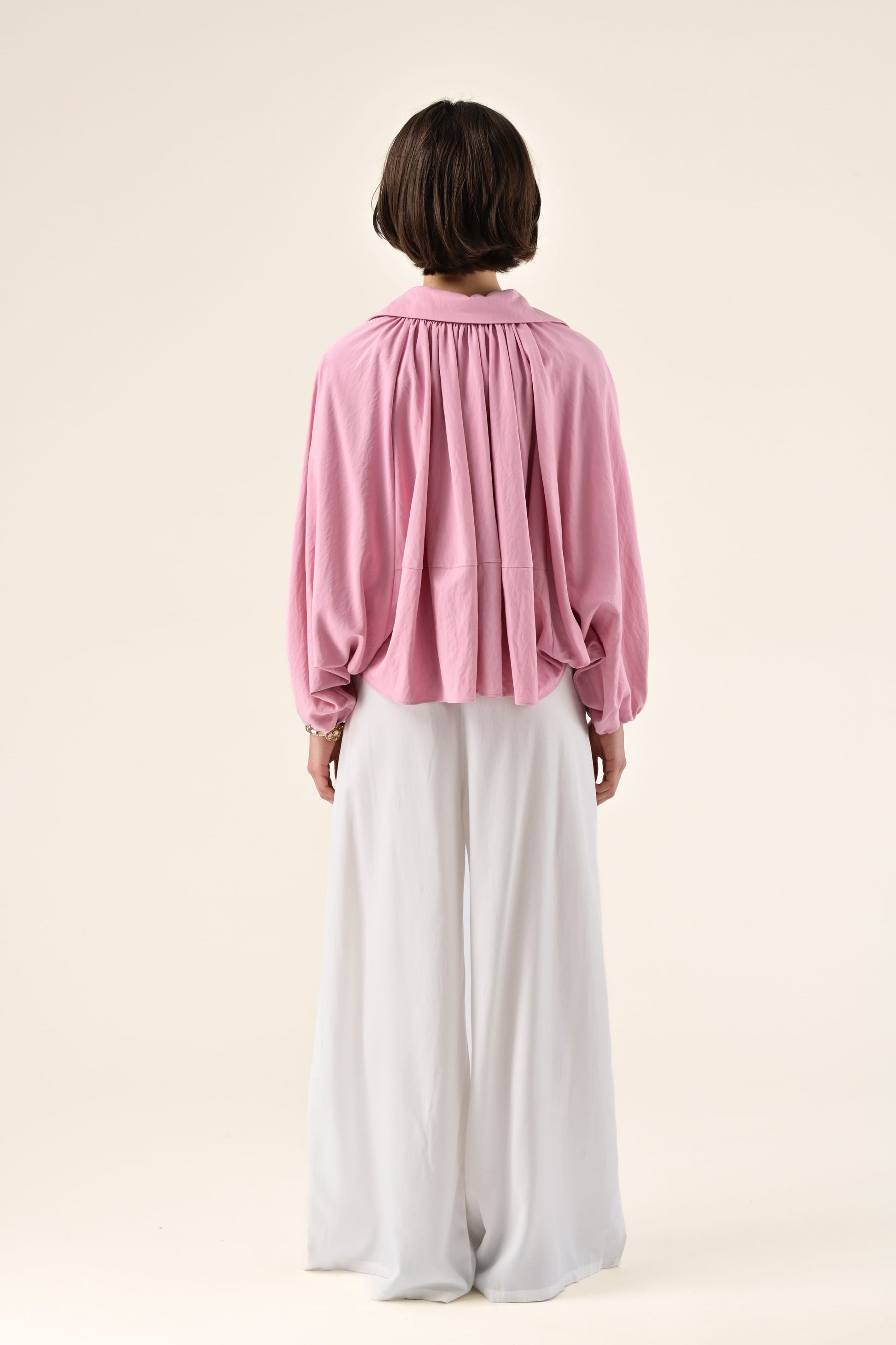 Person wearing a pink blouse and white pants on a light background