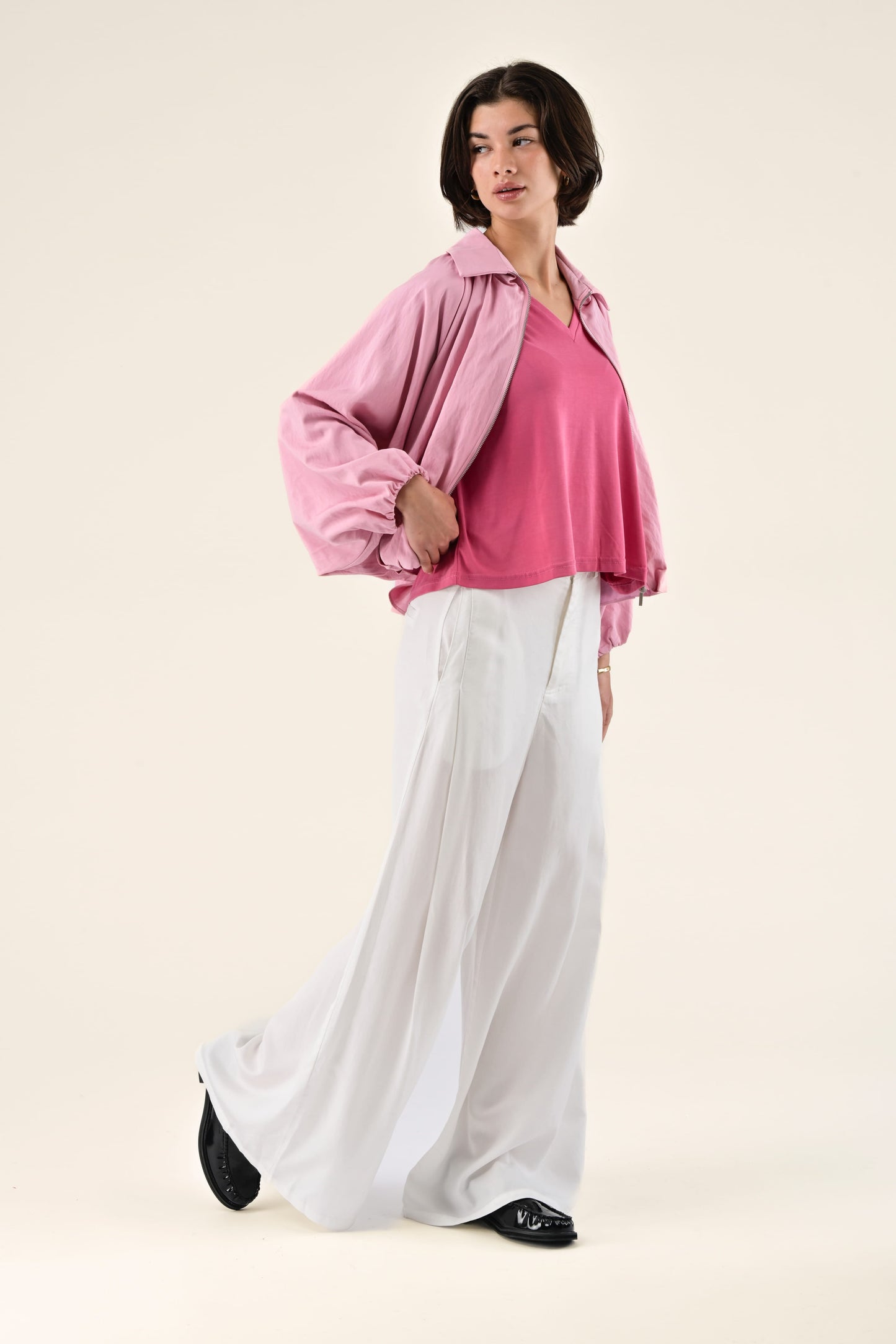 Woman wearing a pink blouse and white pants on a beige background