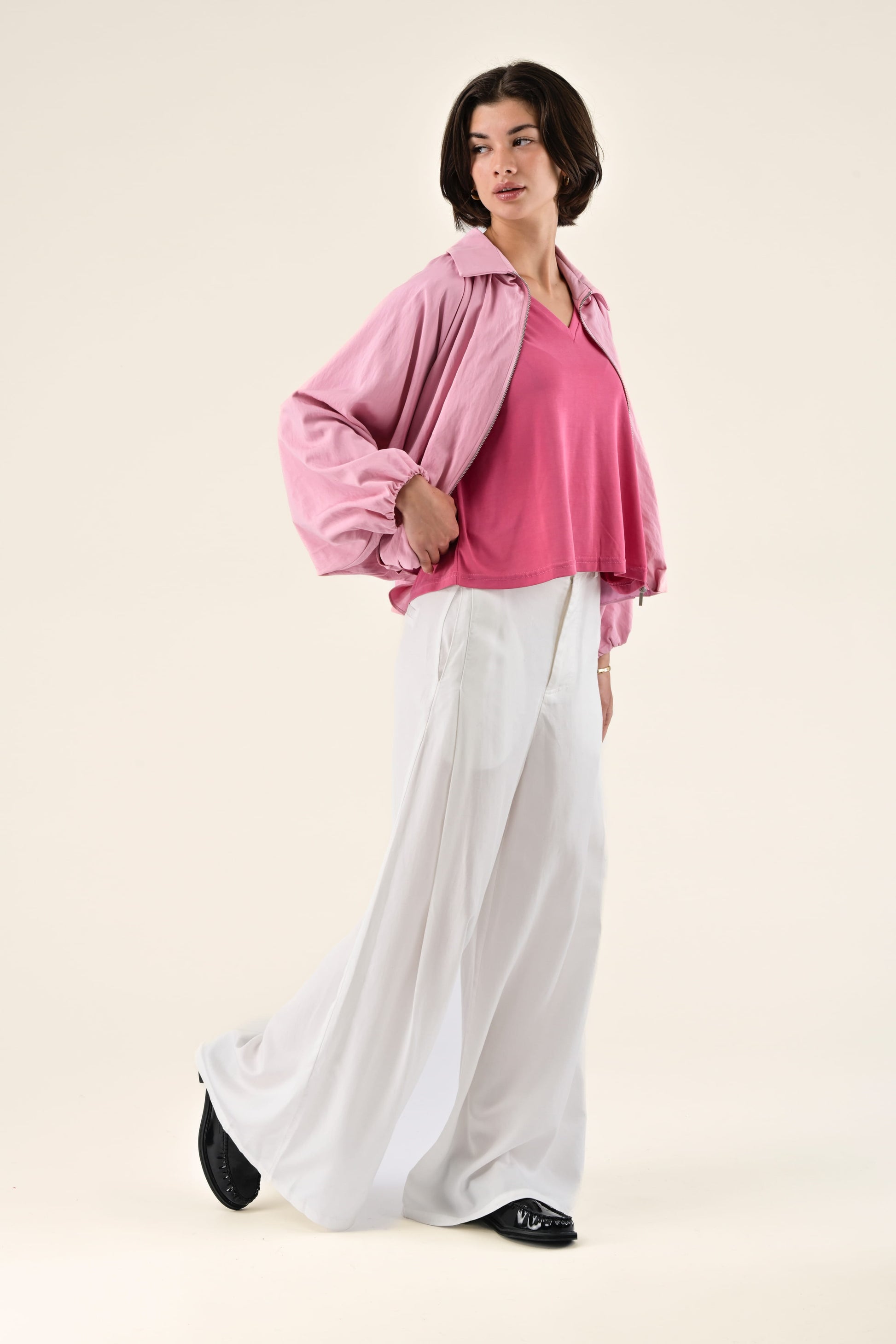 Woman wearing a pink blouse and white pants on a beige background