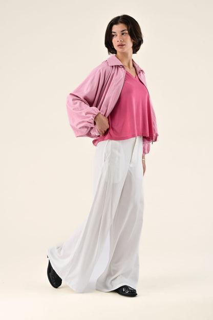 Woman wearing a pink blouse and white pants on a beige background