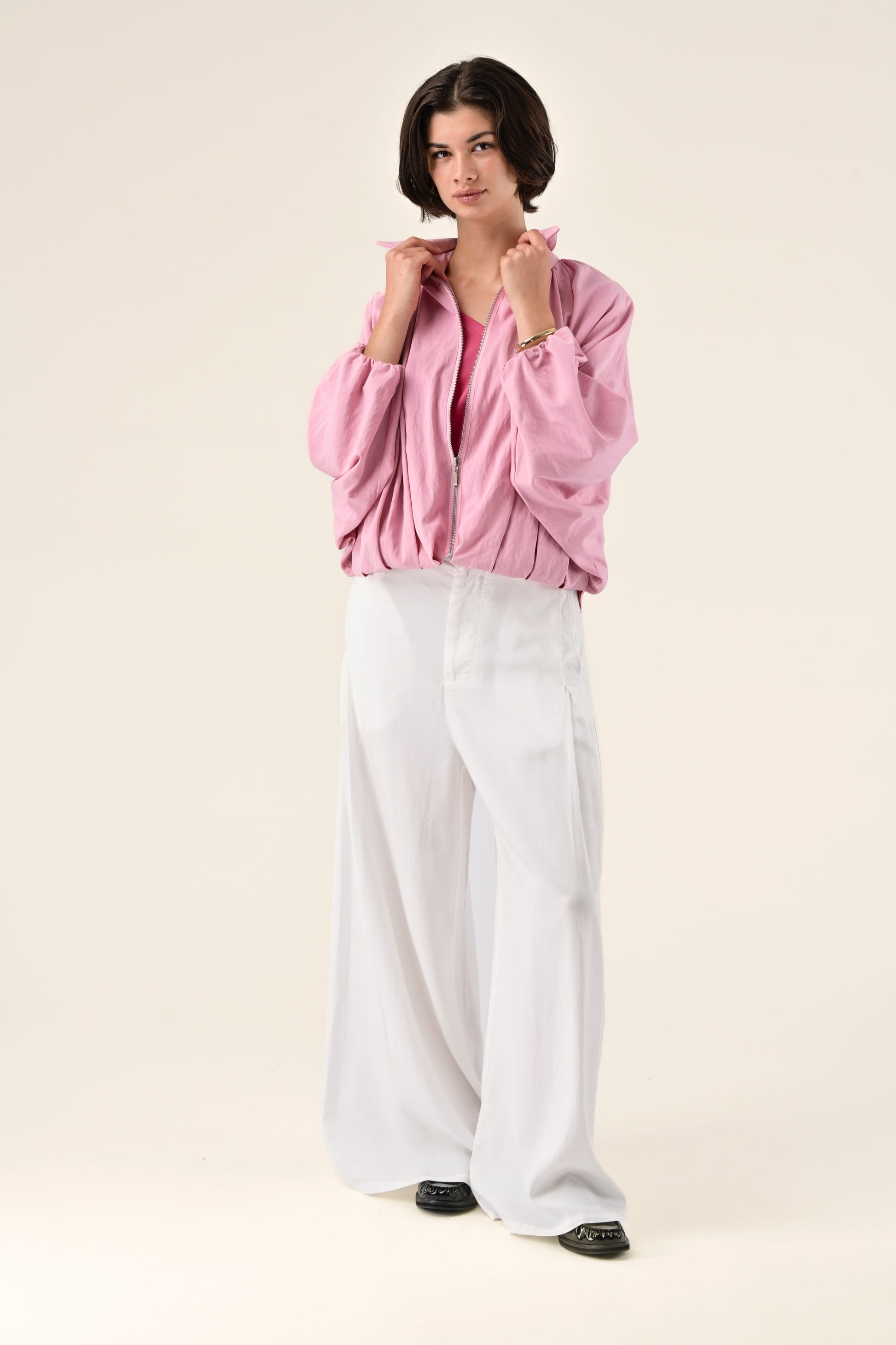 Woman wearing a pink jacket and white pants on a beige background