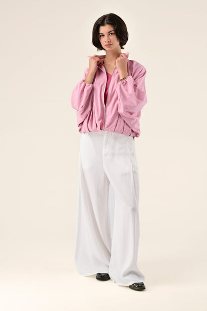Woman wearing a pink jacket and white pants on a beige background